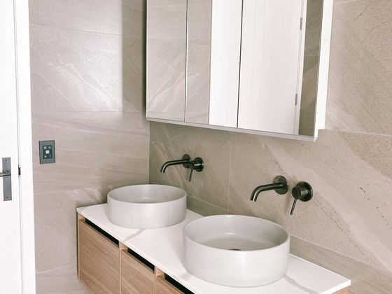 Twin white vessel basins on a timber vanity with black wall-mounted tapware, below a mirrored wall cabinet in a tiled bathroom.
