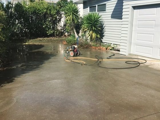 Standing water across a concrete driveway next to a garage, with a hose and a pump running to clear it.