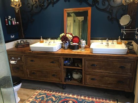 A wider view of the same navy bathroom, showing the timber vanity, a patterned rug, the glass shower and a high-level cistern toilet.